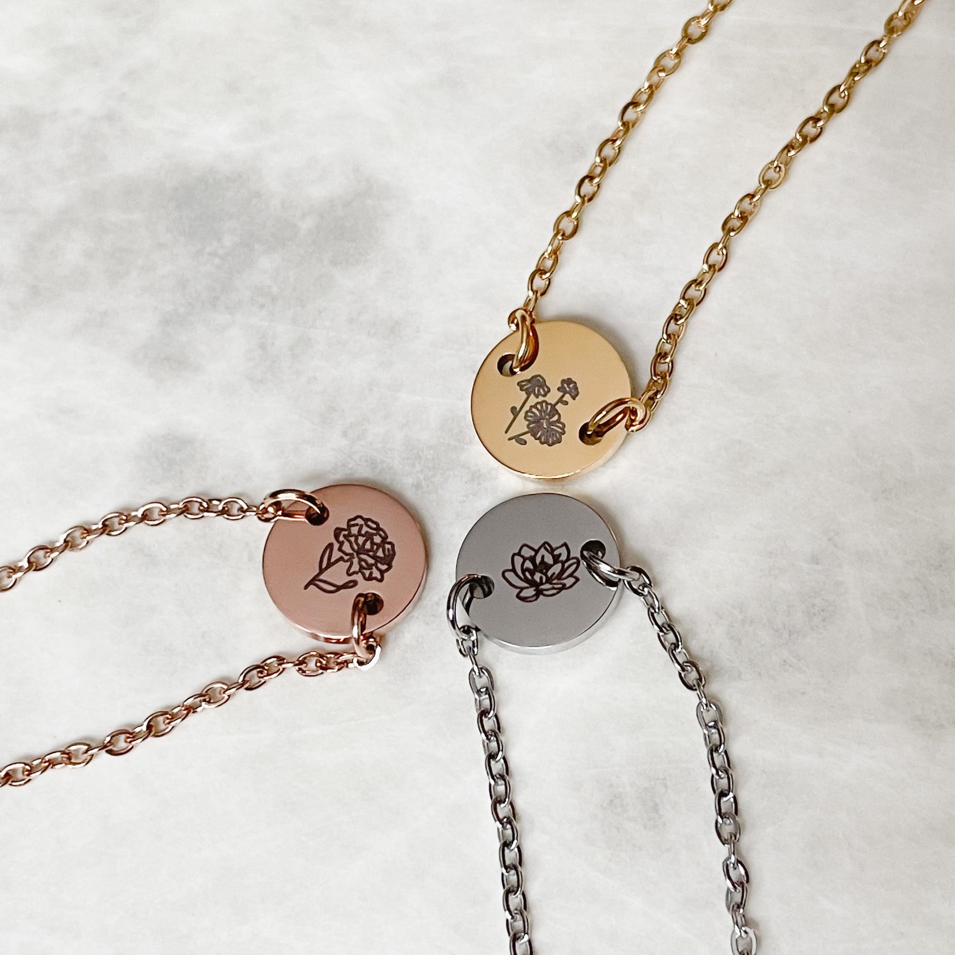 Top view of rose gold, gold and silver  birth flower bracelets with engraved discs on a light background