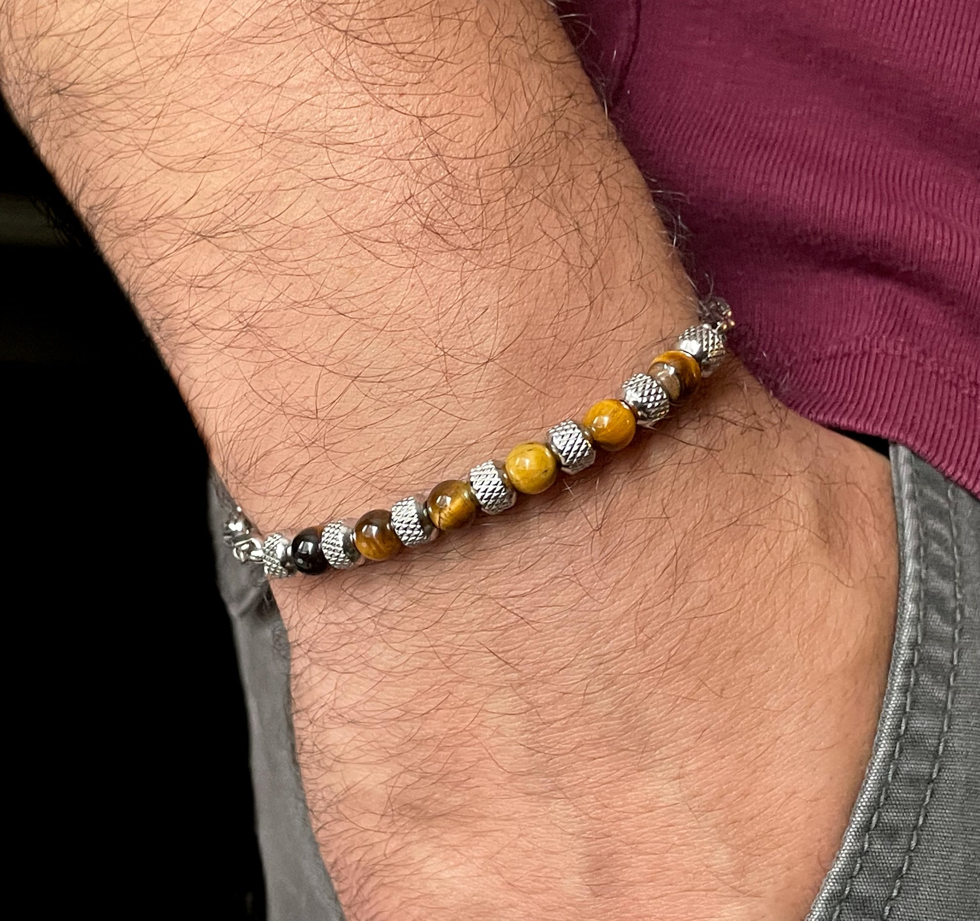 Close-up of a wrist wearing a  brown beaded silver chain bracelet with tiger eye stones and textured steel beads