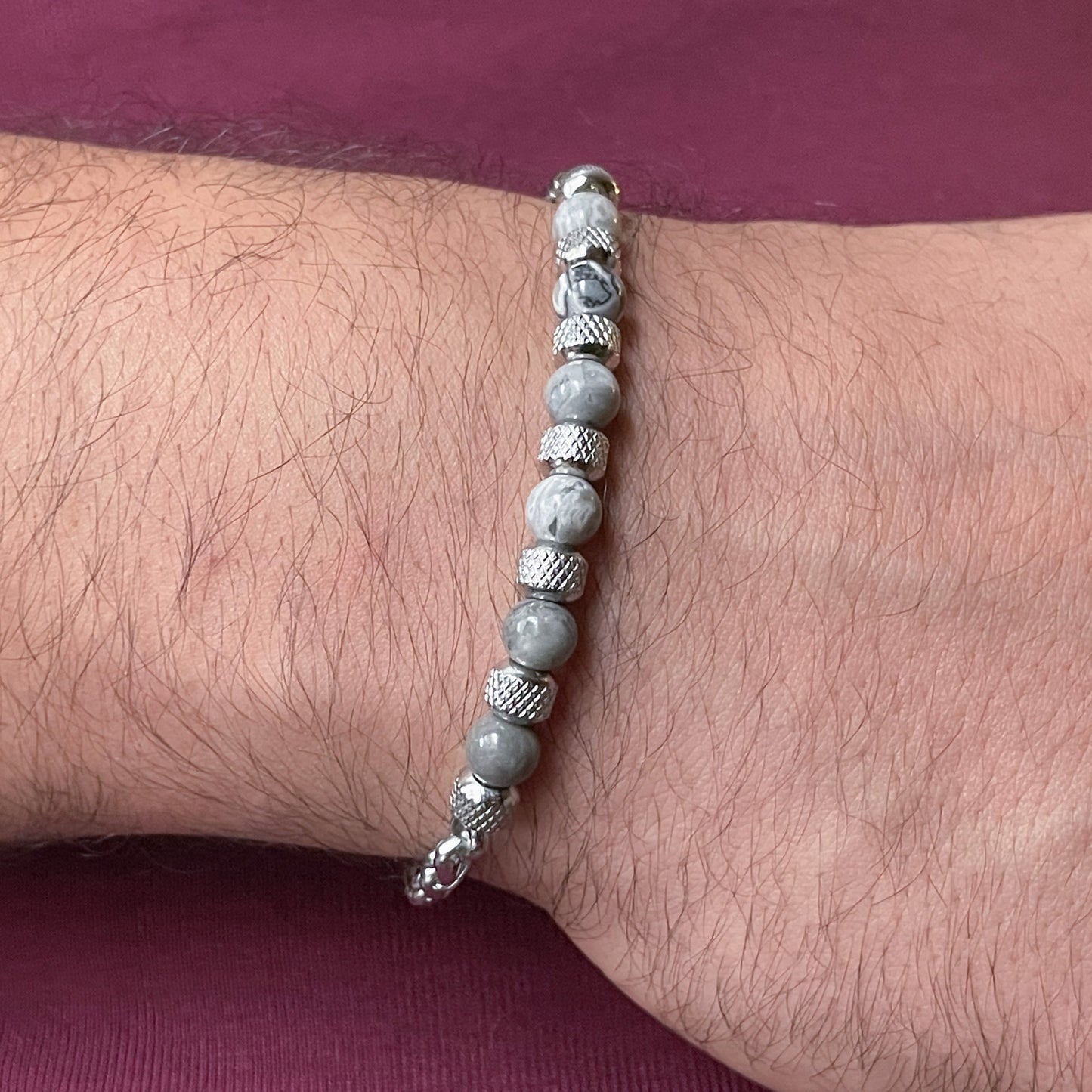 Gray map stone beaded bracelet on a man's wrist with a maroon background