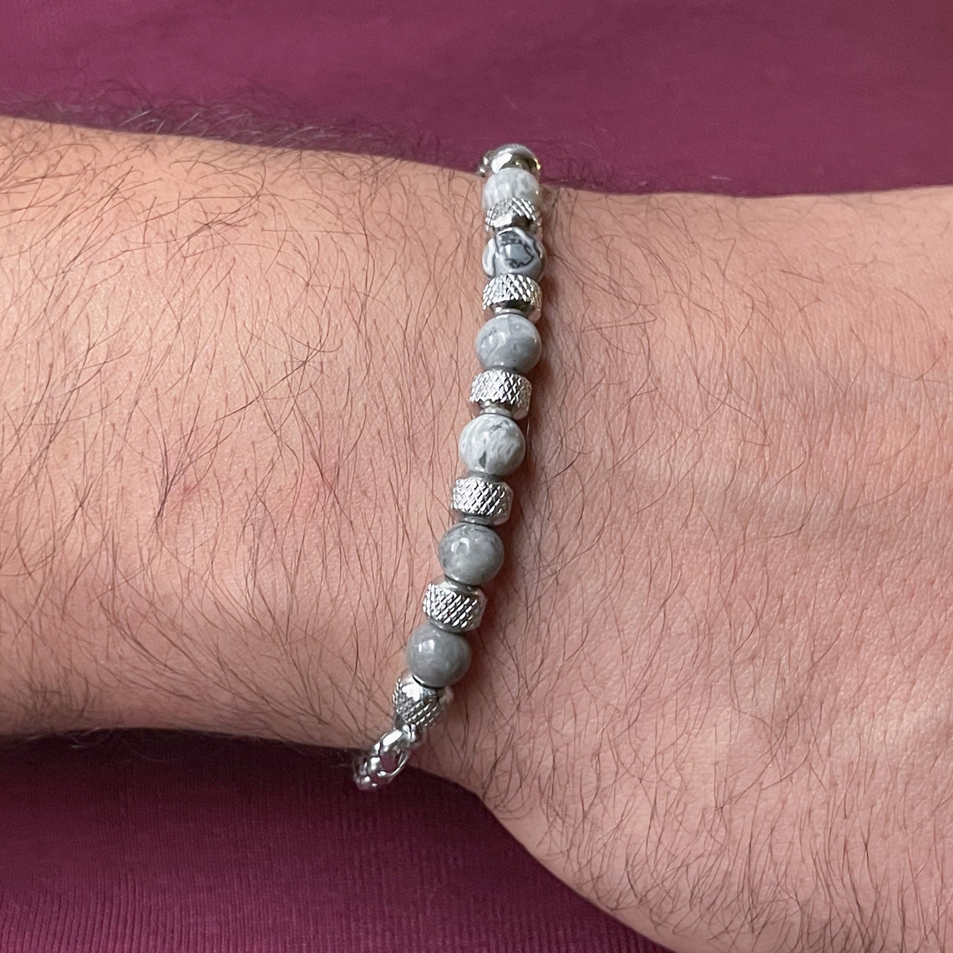 Gray map stone beaded bracelet on a man's wrist with a maroon background