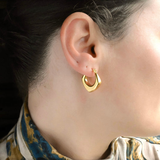 Chunky gold  rhombus hoop earrings on a person against black background