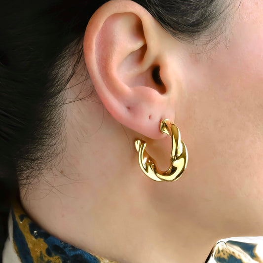 Chunky twisted gold hoop earrings worn by a person