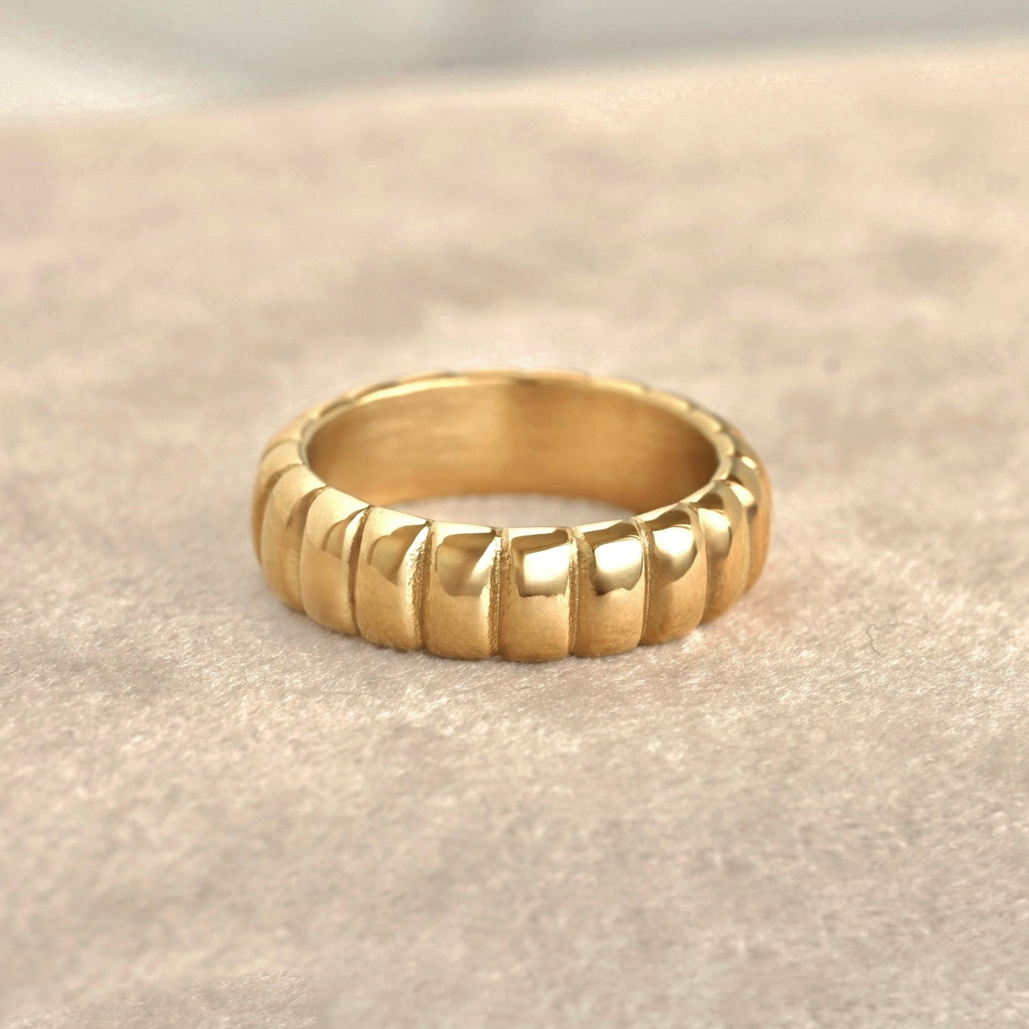 Gold ring with a textured band on a light beige background