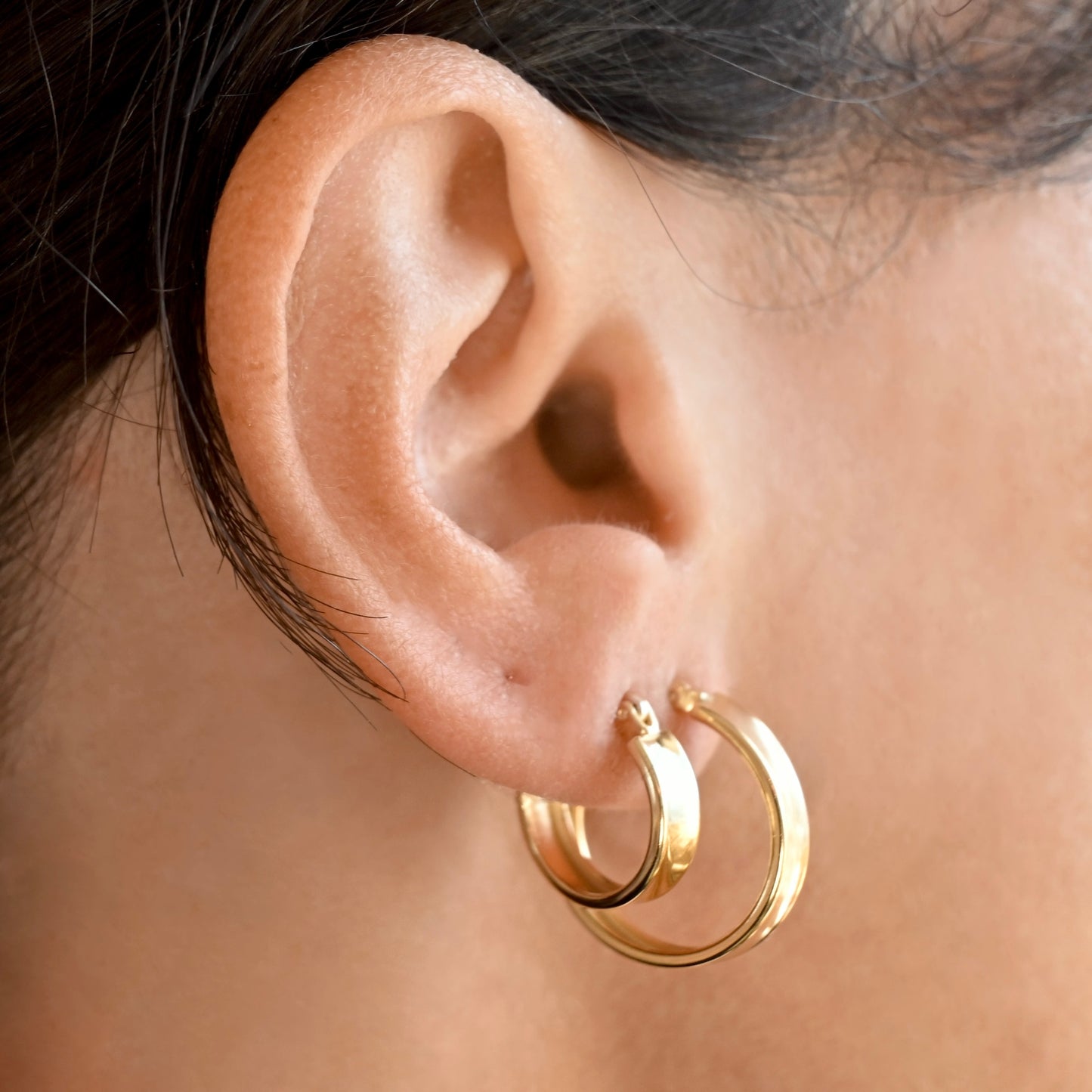 A close-up of a person's ear wearing a pair of gold hoop earrings, one small and one medium.