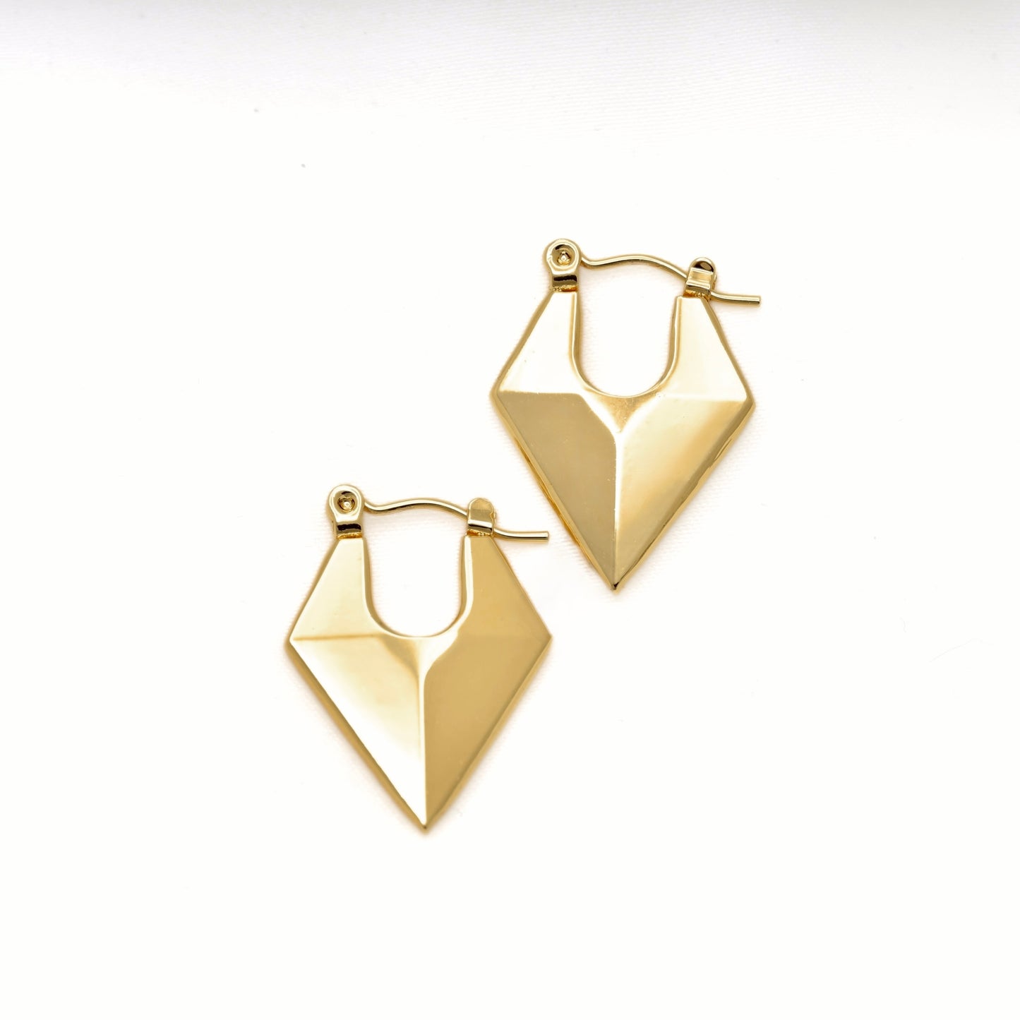 A pair of gold rhombus-shaped hoop earrings with faceted, angular shapes andlatch back clasp, displayed on a clean white background.
