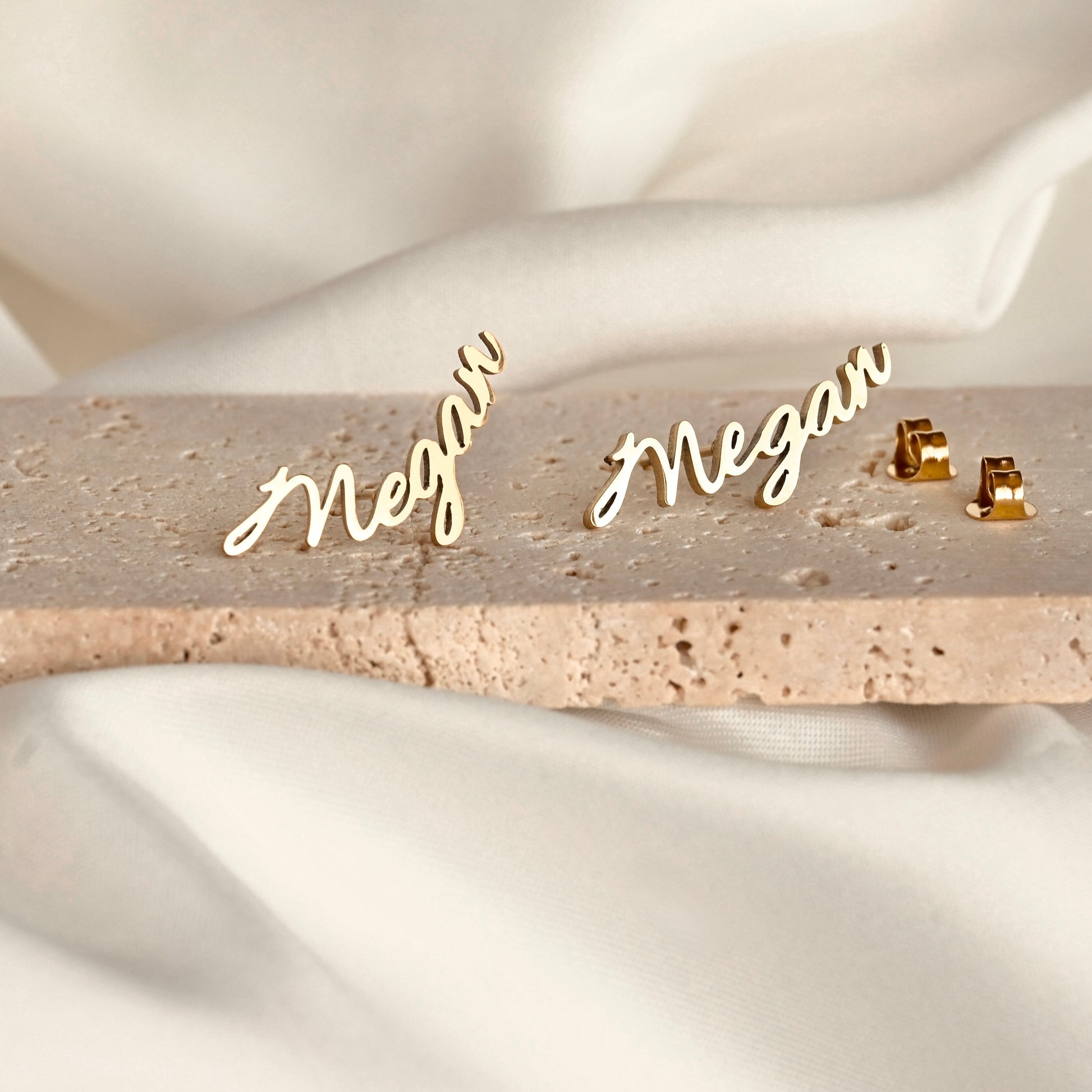 Gold script earrings on a beige stone.