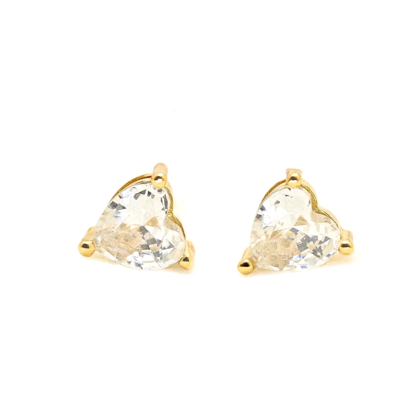 A pair of gold stud earrings featuring heart-shaped clear gemstones in a three-prong setting, shown against a plain white background.