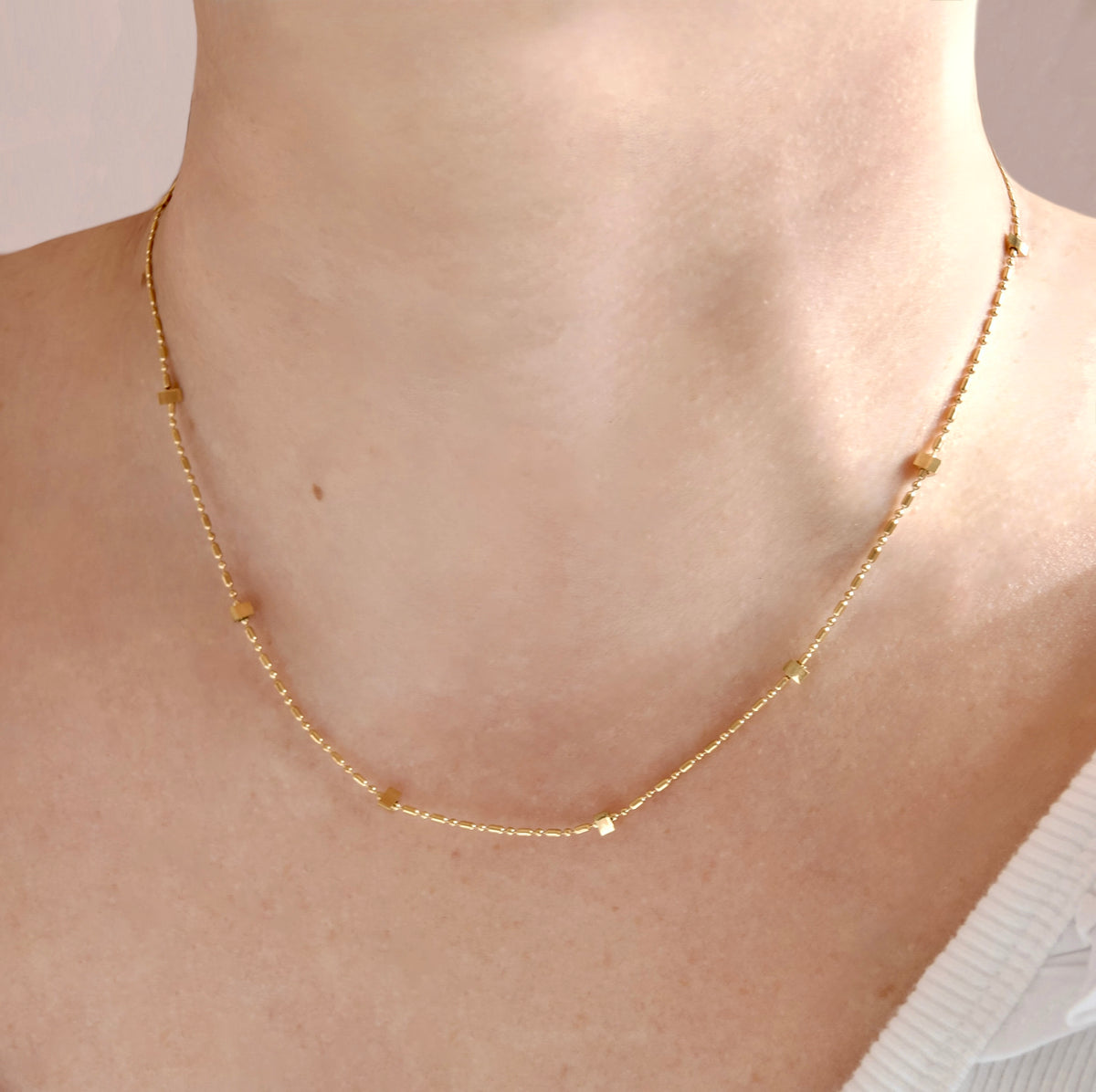 A delicate gold chain necklace with small spaced beads, worn on a model's neck.