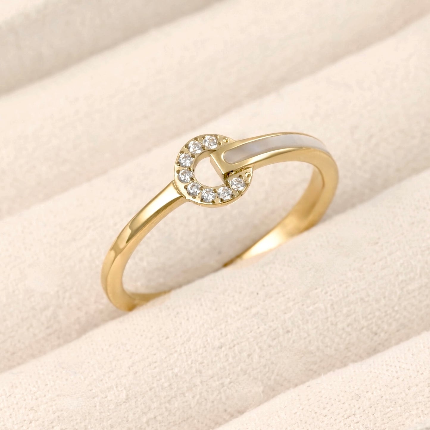 Gold circle ring adorned with cz stones and shell inlay on one side of the band, displayed in a beige jewelry box.