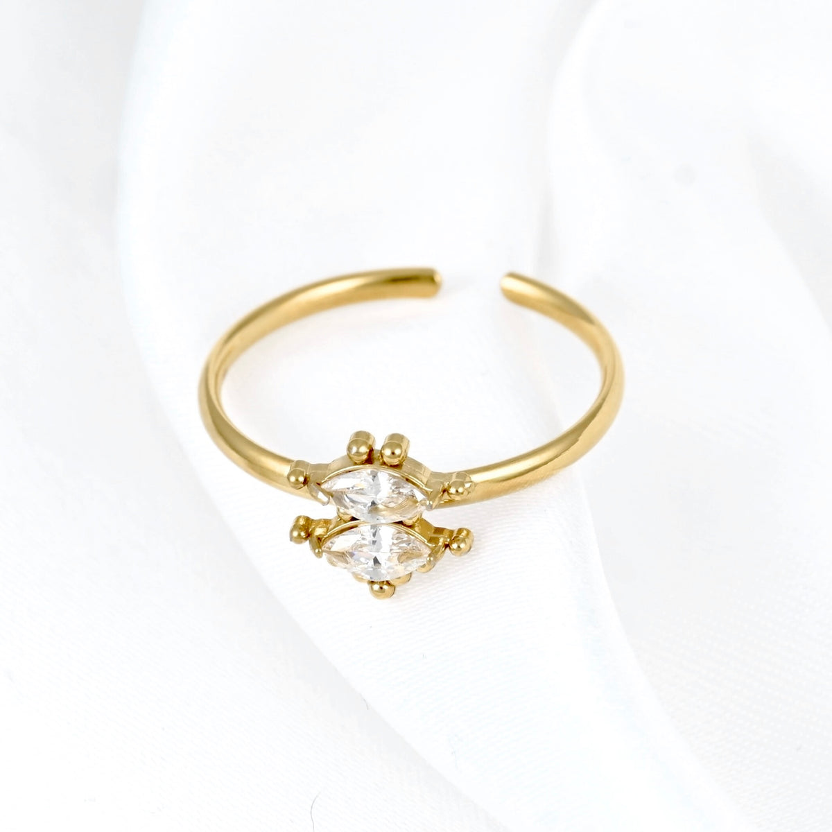 A gold adjustable ring featuring a marquise-cut clear gemstone in a prong setting, displayed on a soft white fabric background.