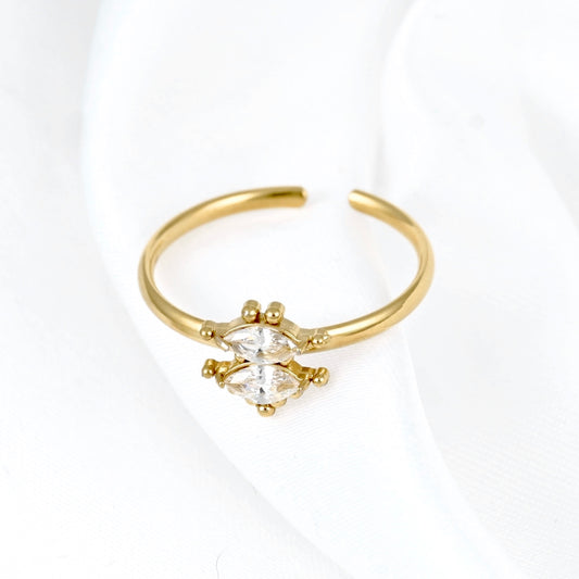 A gold adjustable ring featuring a marquise-cut clear gemstone in a prong setting, displayed on a soft white fabric background.