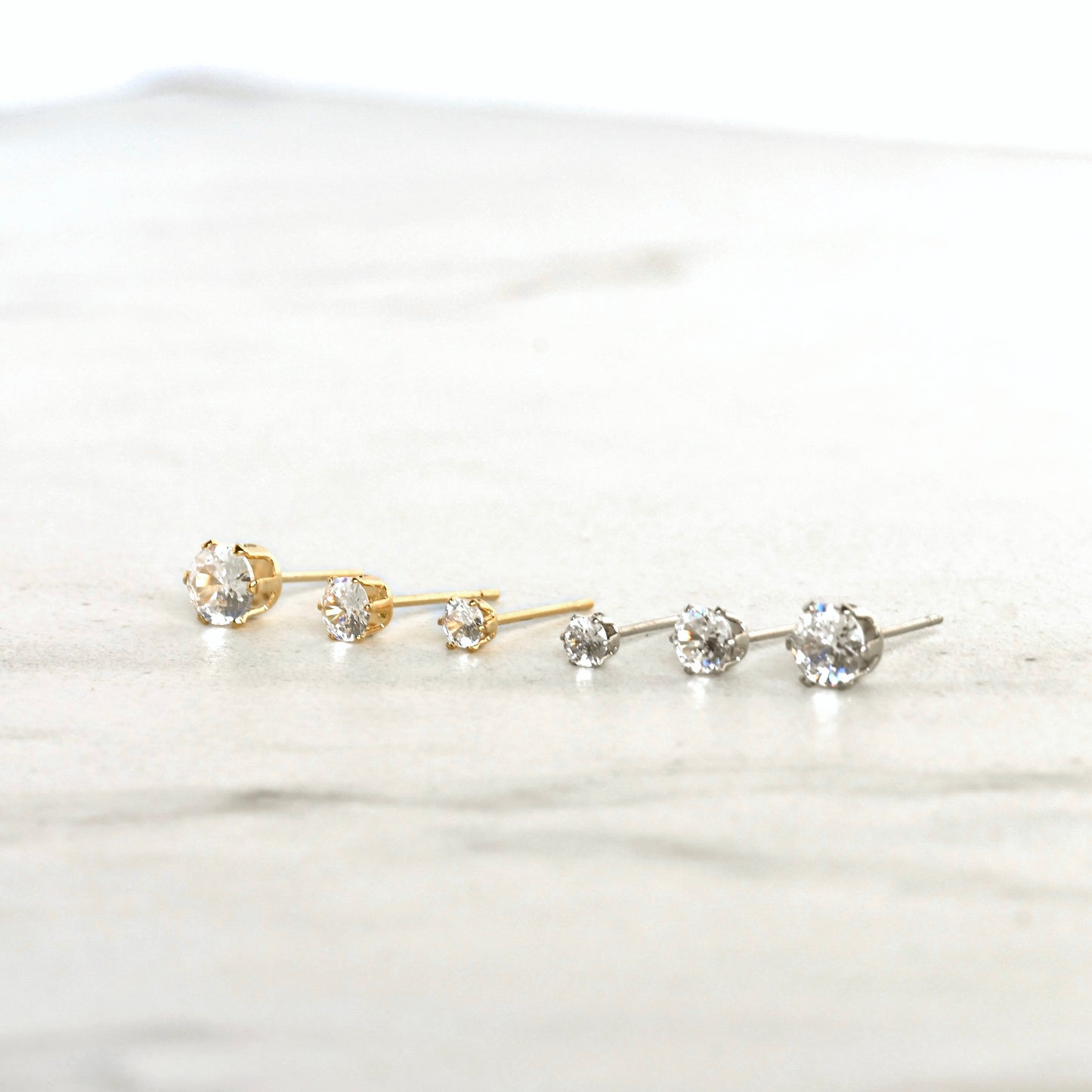 Gold and silver stud earrings with clear CZ stones on a white background