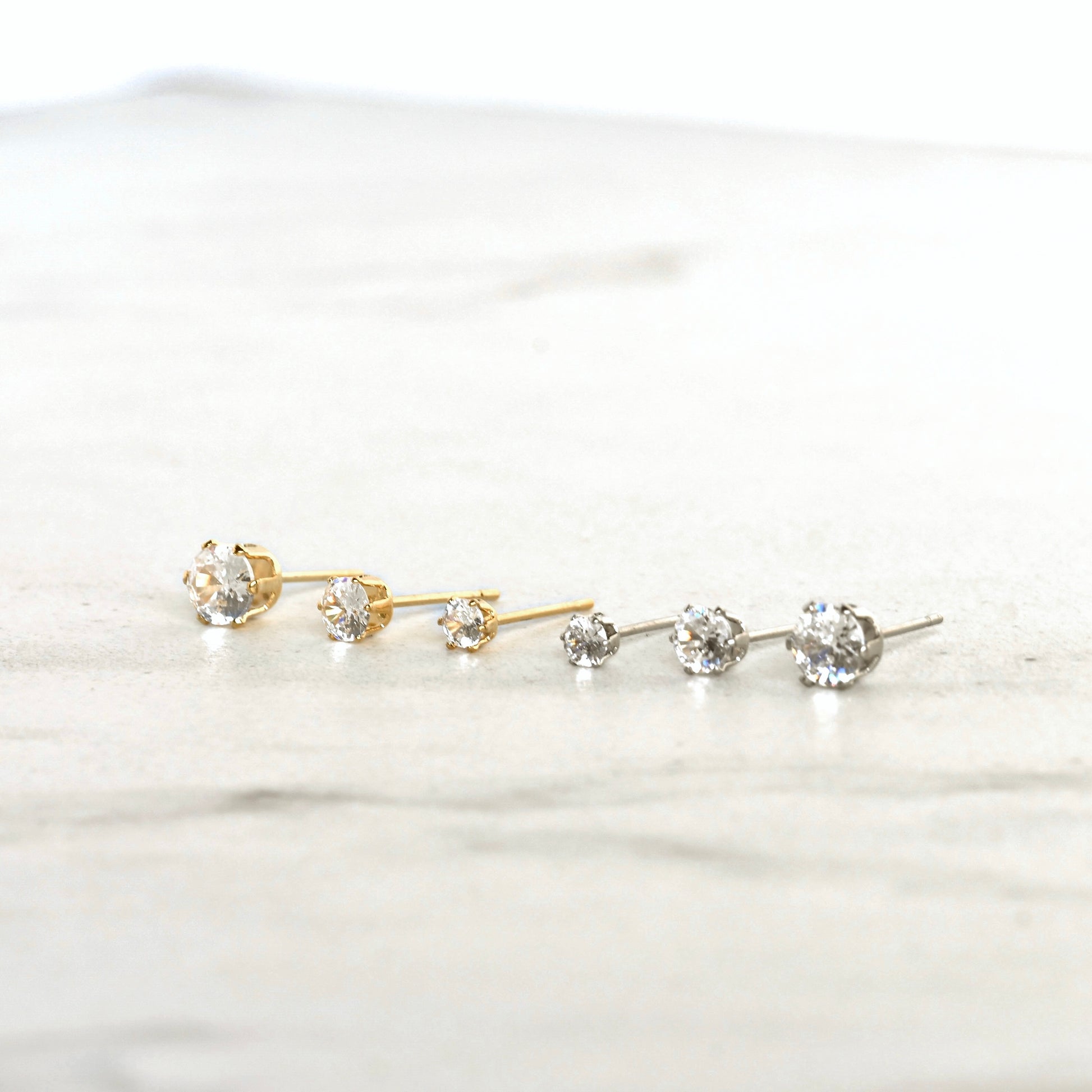 Gold and silver stud earrings with clear CZ stones on a white background