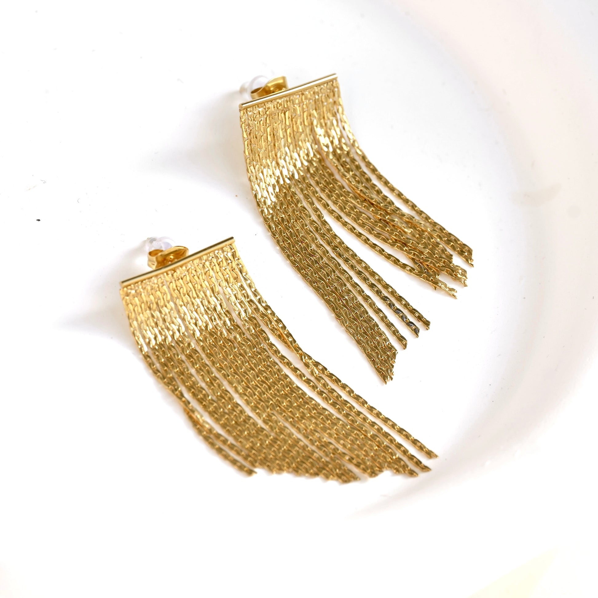 A pair of gold-toned fringe earrings with a textured, woven chain-like design, displayed on a clean white background.