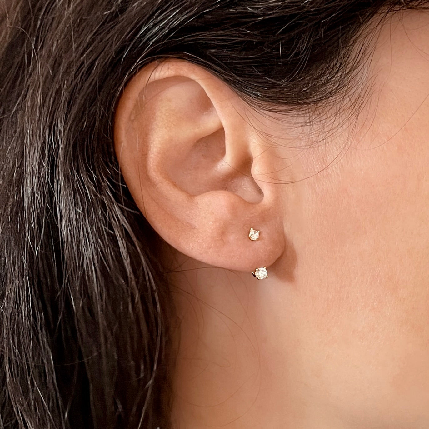 Close up of a model's ear wearing a fron-back round stud earrings in gold 