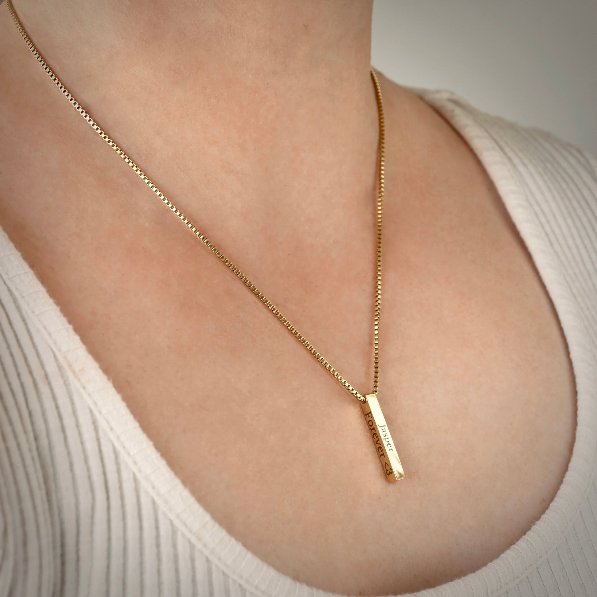 Gold engraved bar necklace with custom  texts on right and front sides on a person wearing a white top
