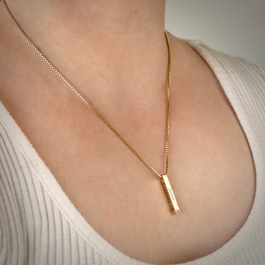 Gold engraved bar necklace with custom  texts on right and front sides on a person wearing a white top