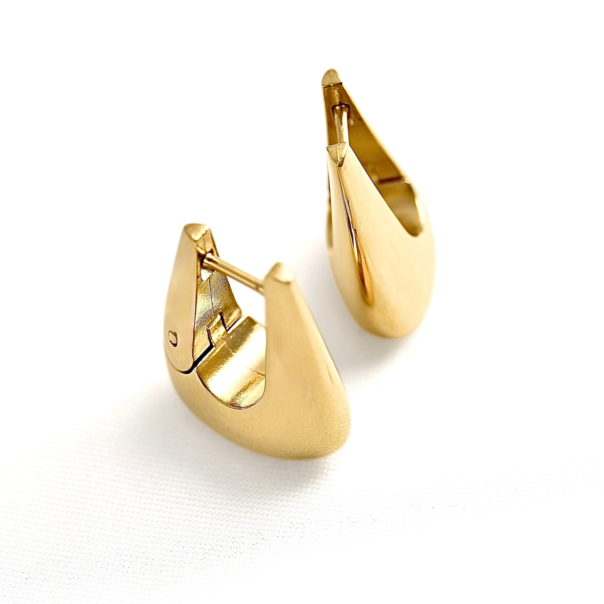 A pair of gold huggie hoop earrings with a polished, reflective finish, displayed on a clean white background.