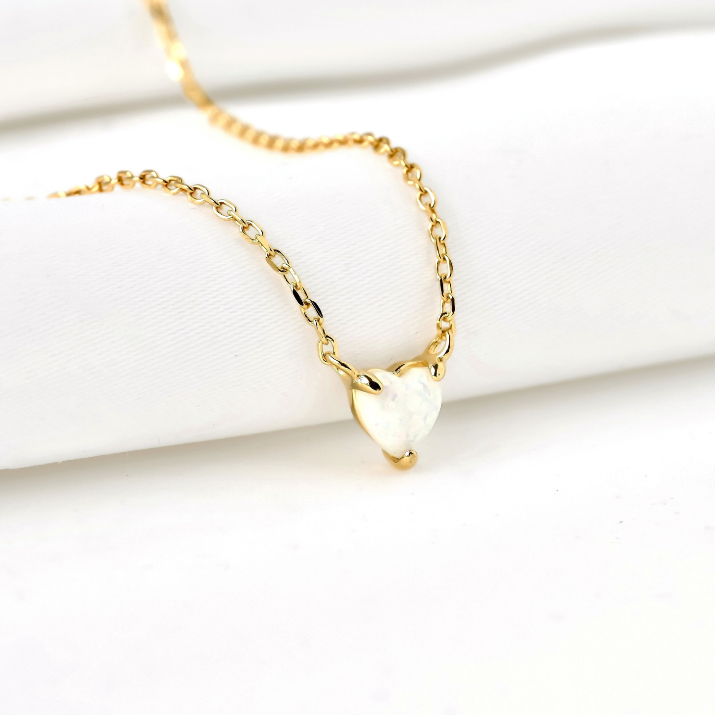 Gold necklace with a heart-cut opal stone pendant on a white surface