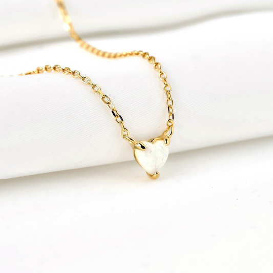 Gold necklace with a heart-cut opal stone pendant on a white surface