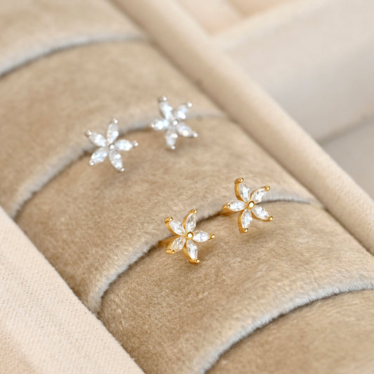 Gold and silver flower earrings with marquise-cut diamonds on a textured beige surface