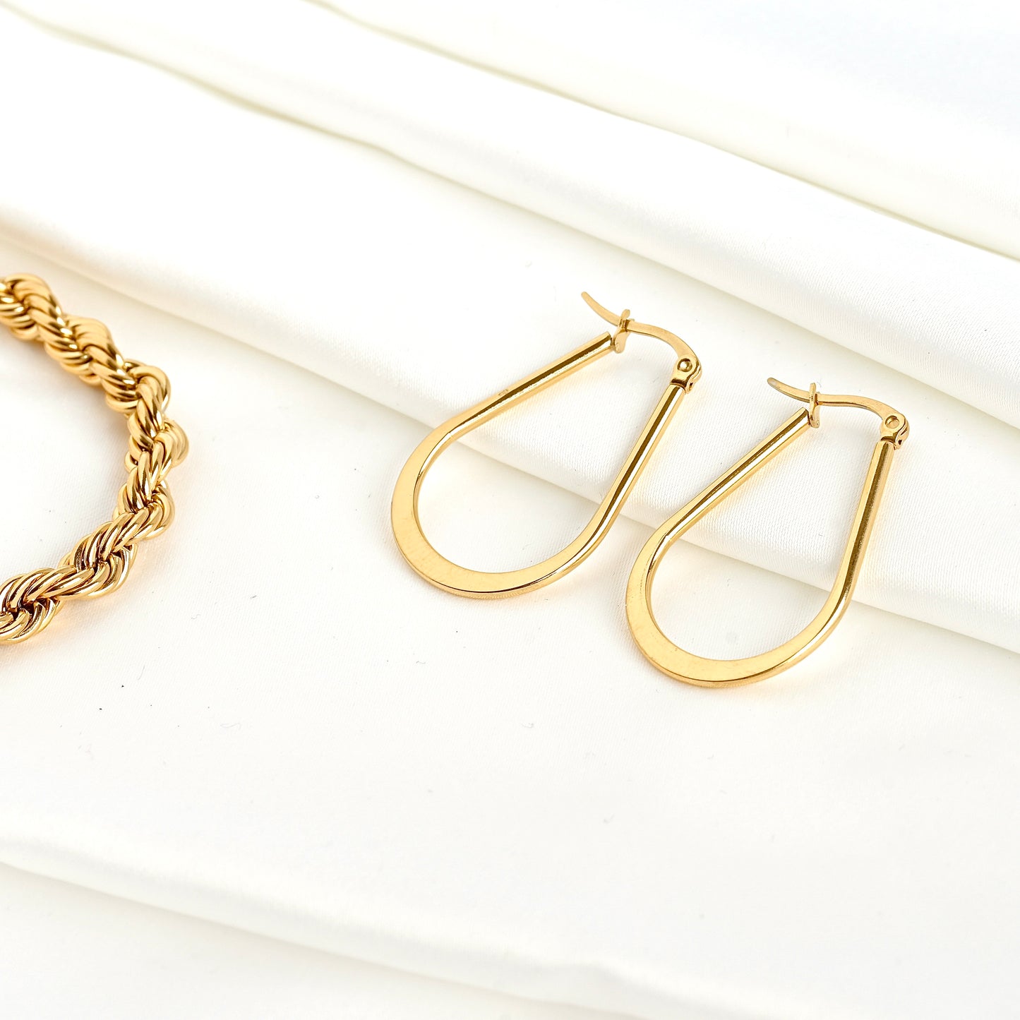 Gold pear shaped hoop earrings with a rope chain prop on a white background
