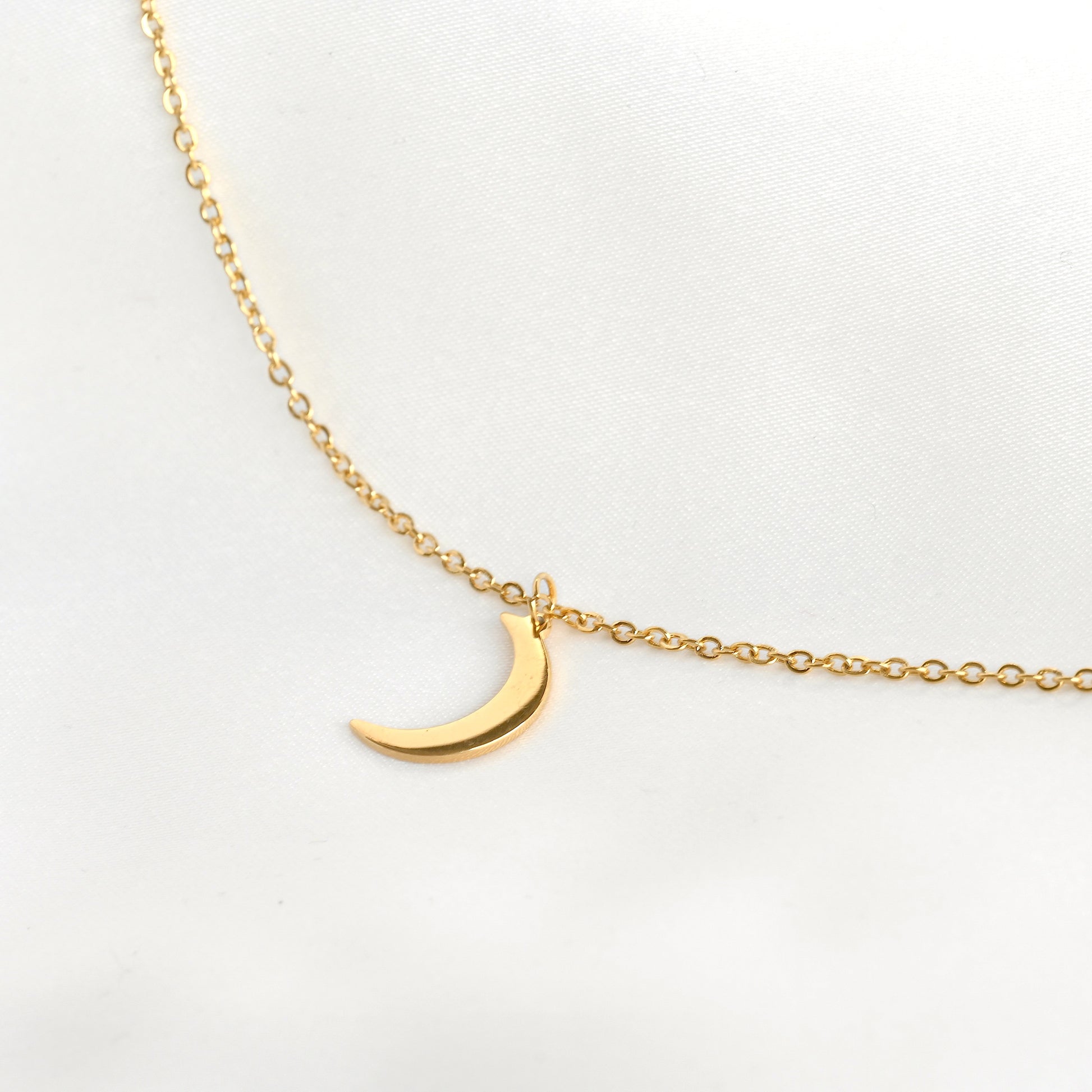 Gold necklace with a crescent moon pendant on a light gray background