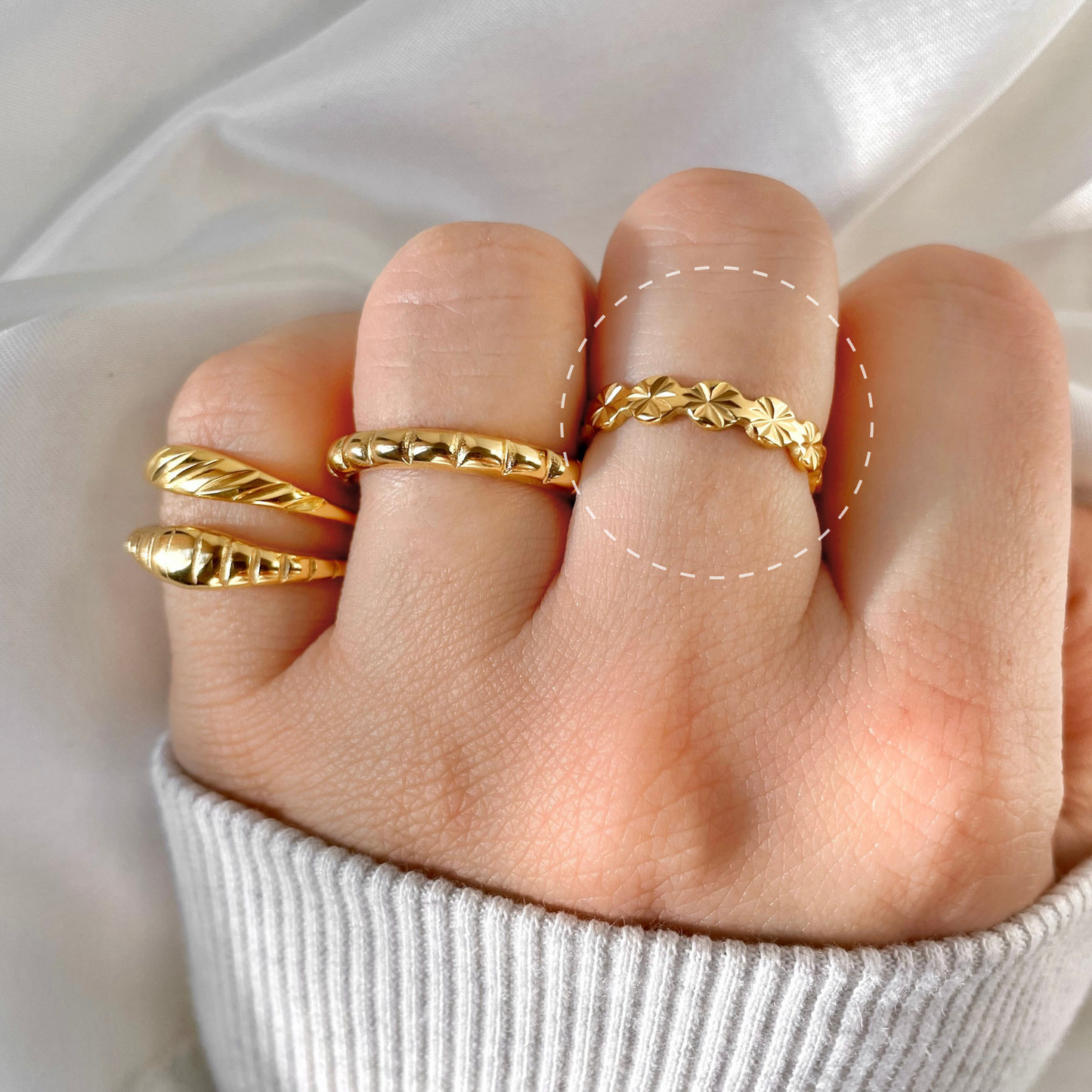 Gold ring stack on a finger against a neutral background