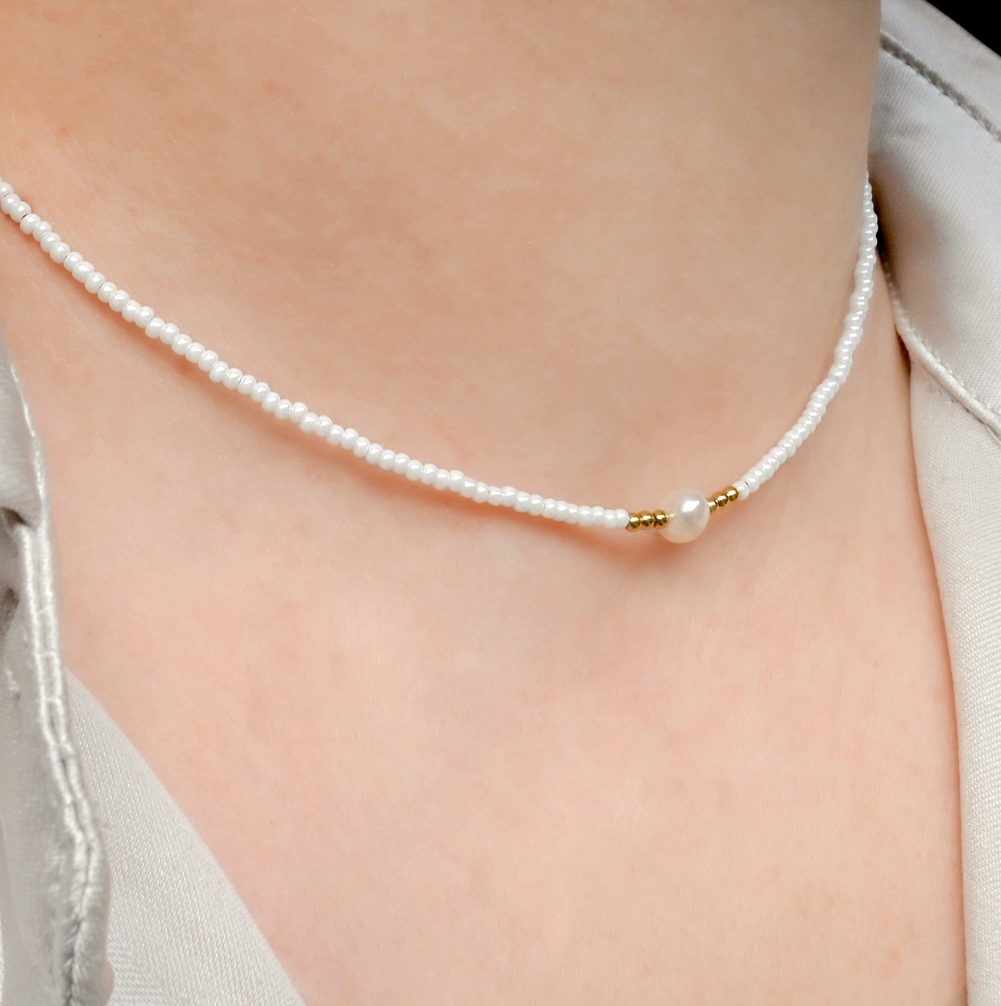White seed bead pearl necklace with gold beads accents on a person wearing a light-colored top.