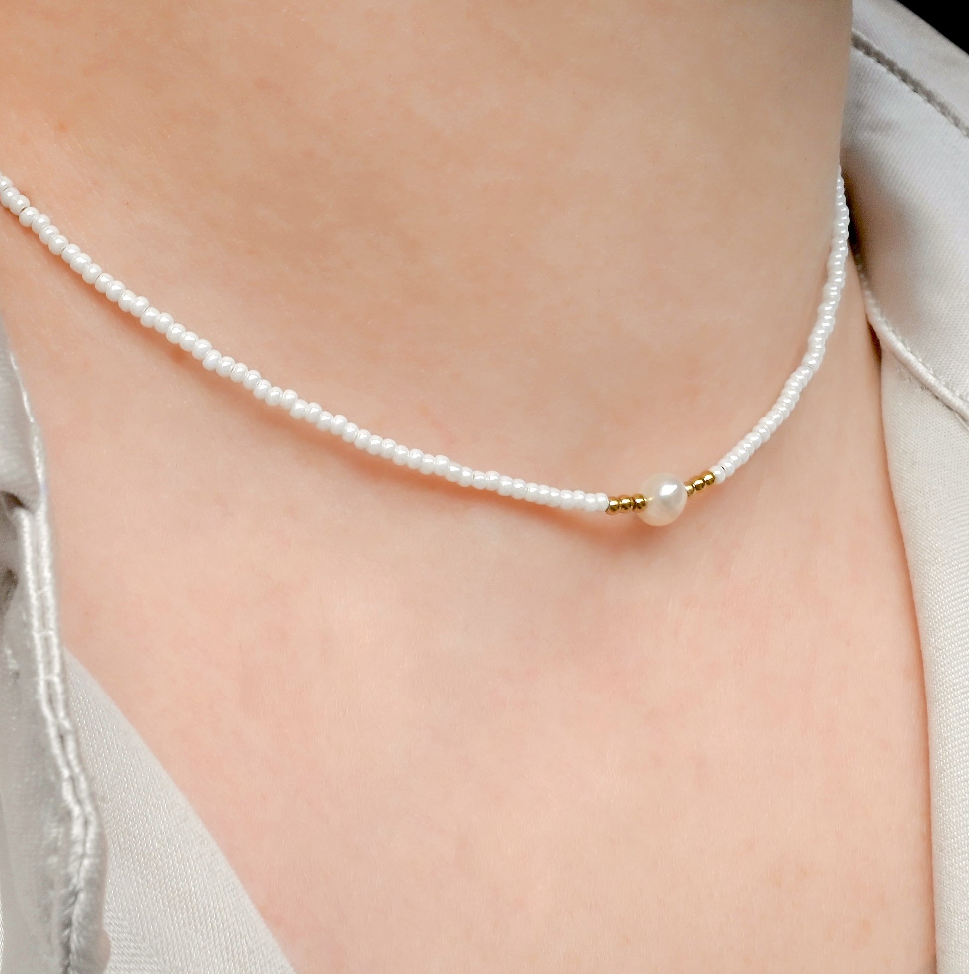 White seed bead pearl necklace with gold beads accents on a person wearing a light-colored top.
