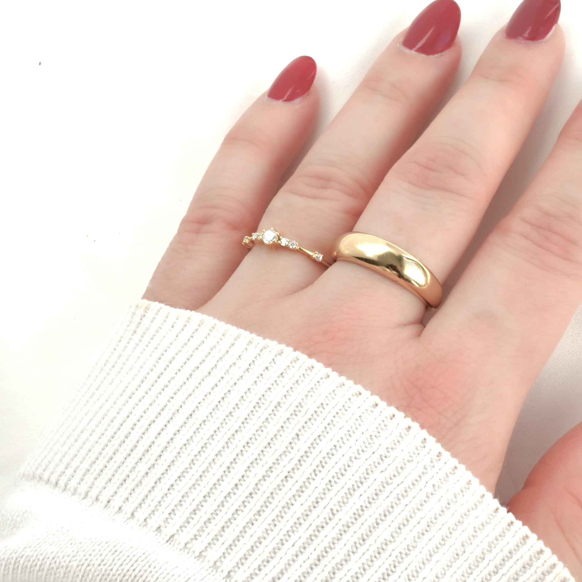 Hand wearing two gold rings, one with diamonds and other chunky dome on a light background