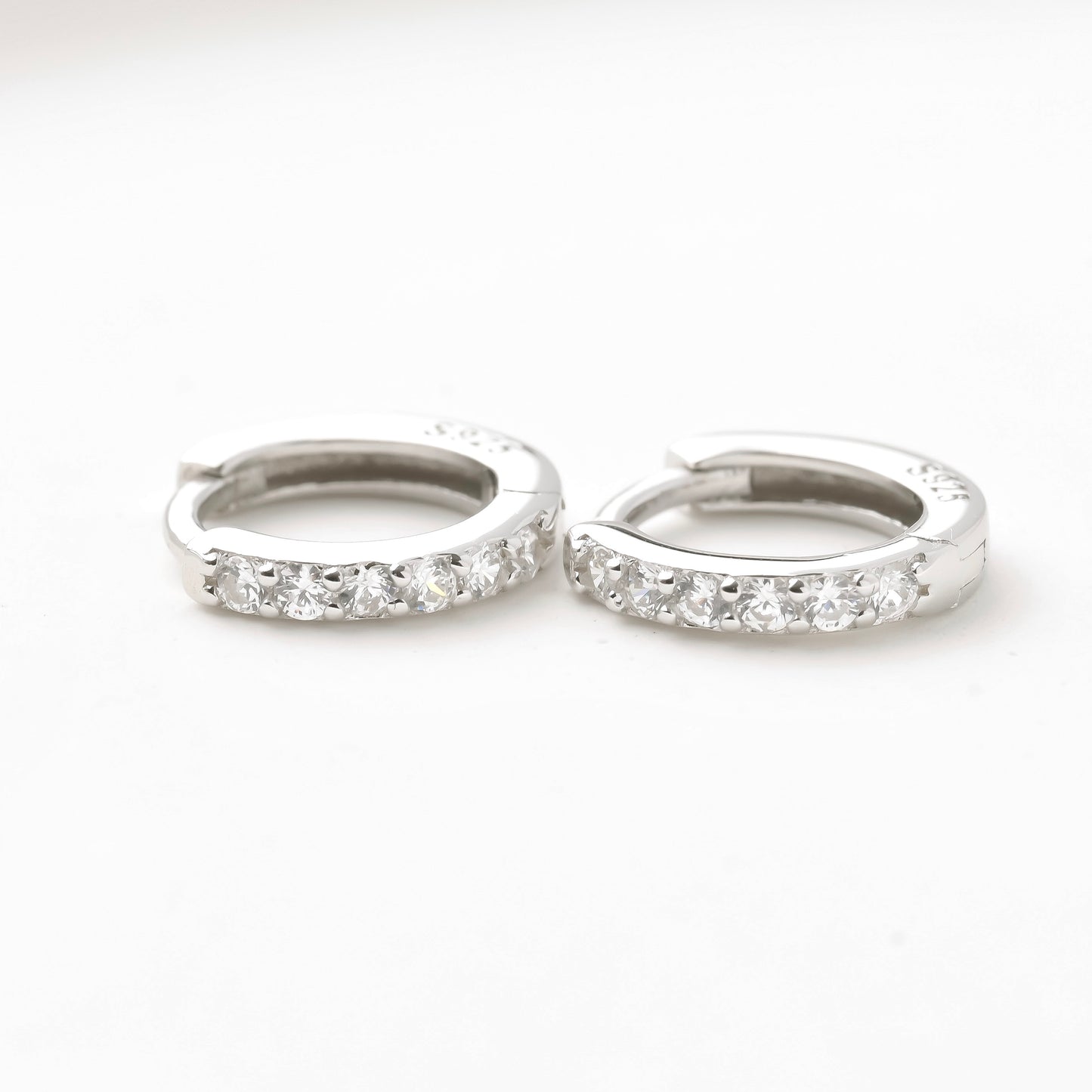 Pair of silver half eternity CZ hoop earrings on a white background