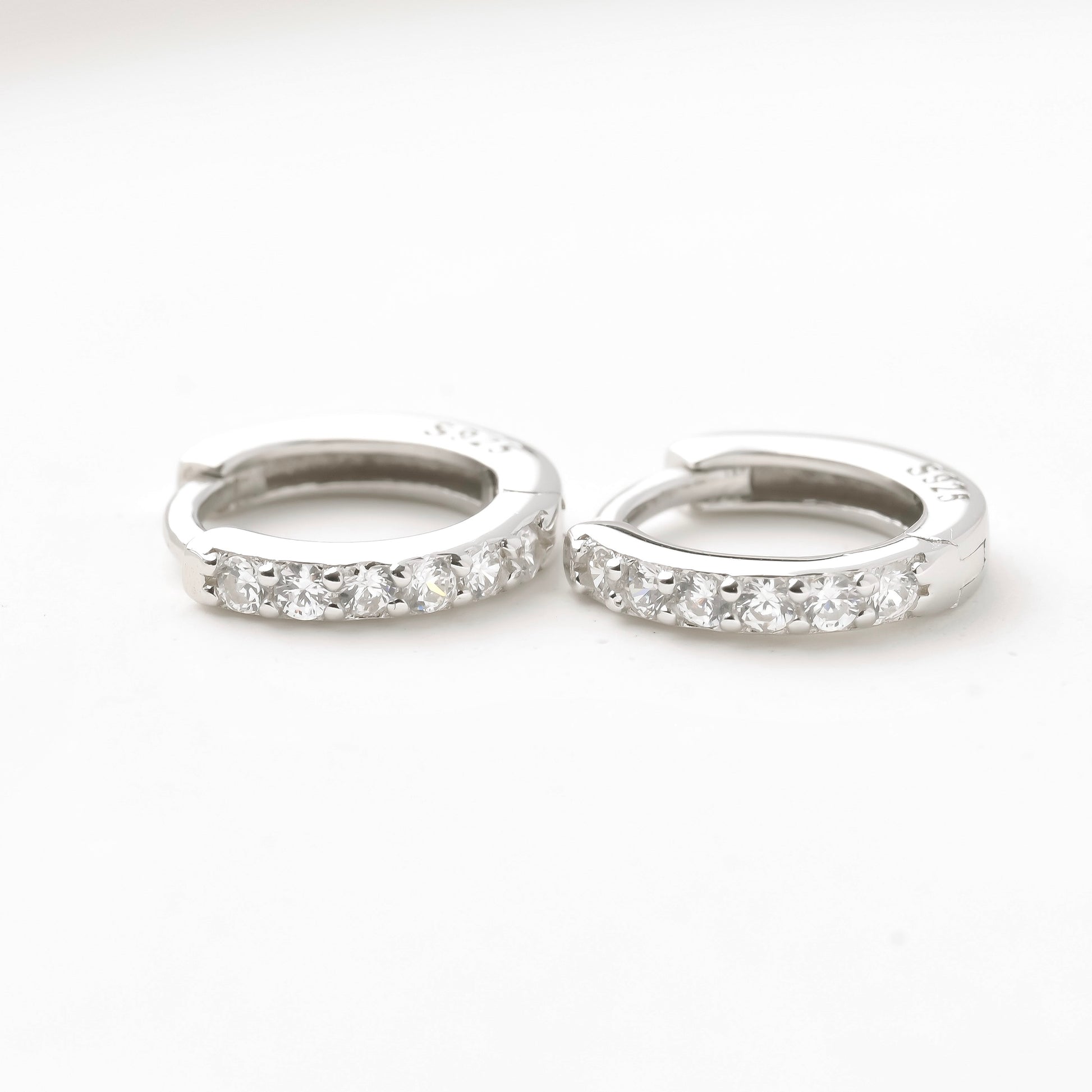 Pair of silver half eternity CZ hoop earrings on a white background