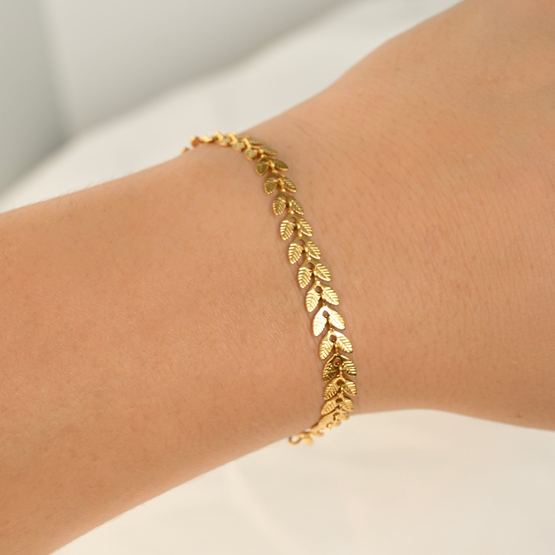 Elegant textured leaf chain bracelet on a wrist against a neutral background