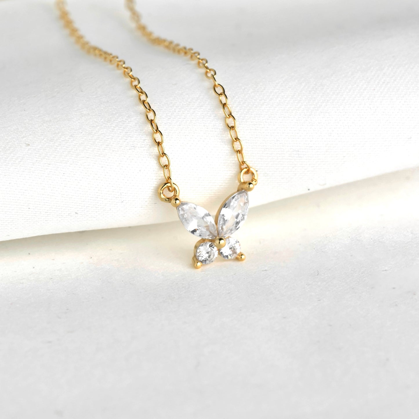 Gold butterfly necklace with clear gemstones on a white background
