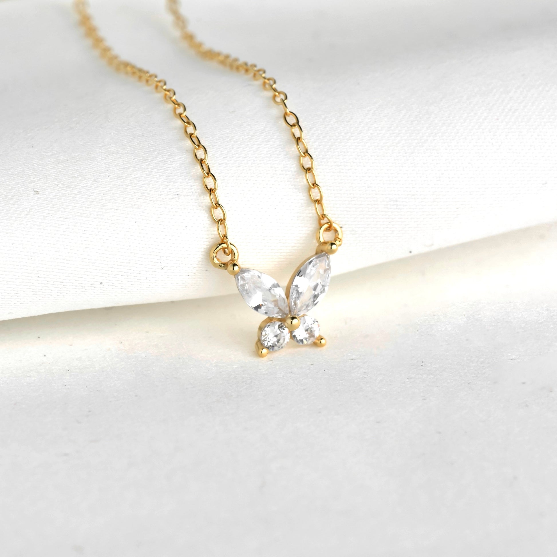 Gold butterfly necklace with clear gemstones on a white background