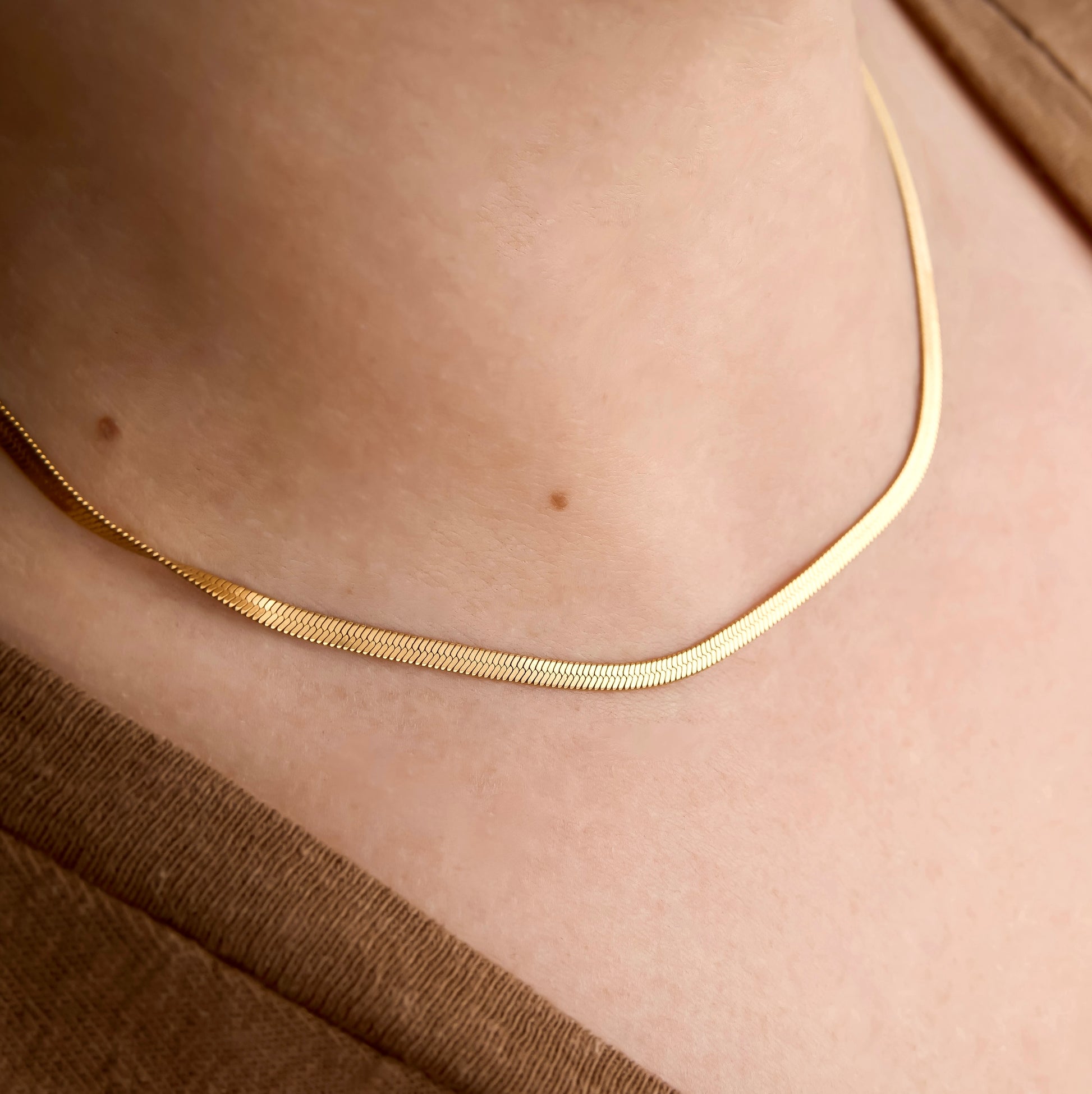 Gold flat snake chain necklace on a person's neck with a neutral background