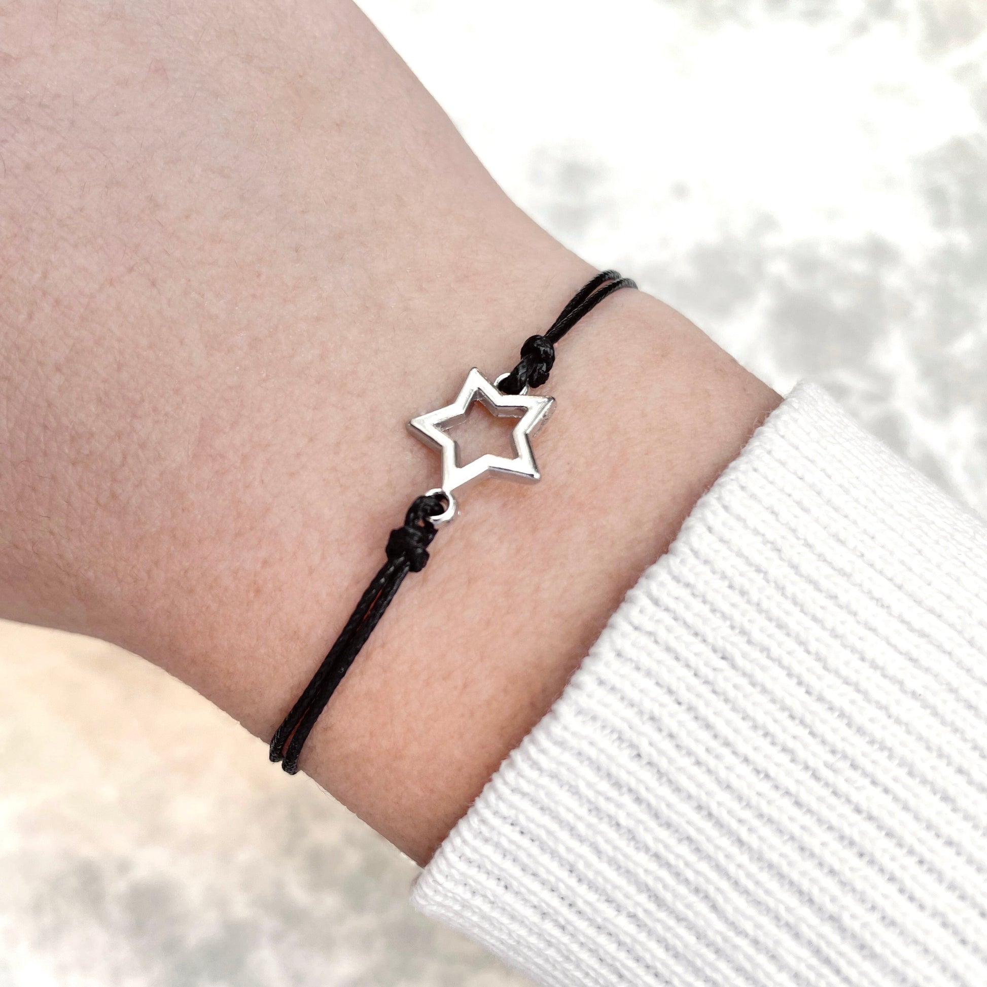Star-shaped bracelet with a black cord on a wrist with a white background