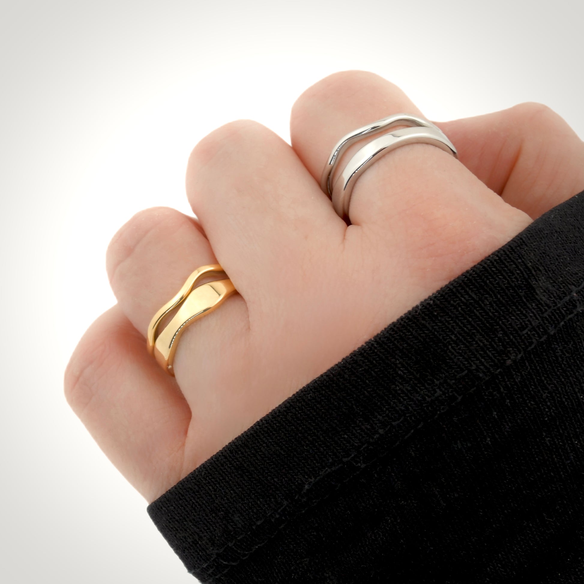 Hand wearing two ring pairs (thin and thick wavy bands) in gold and silver, on a white background