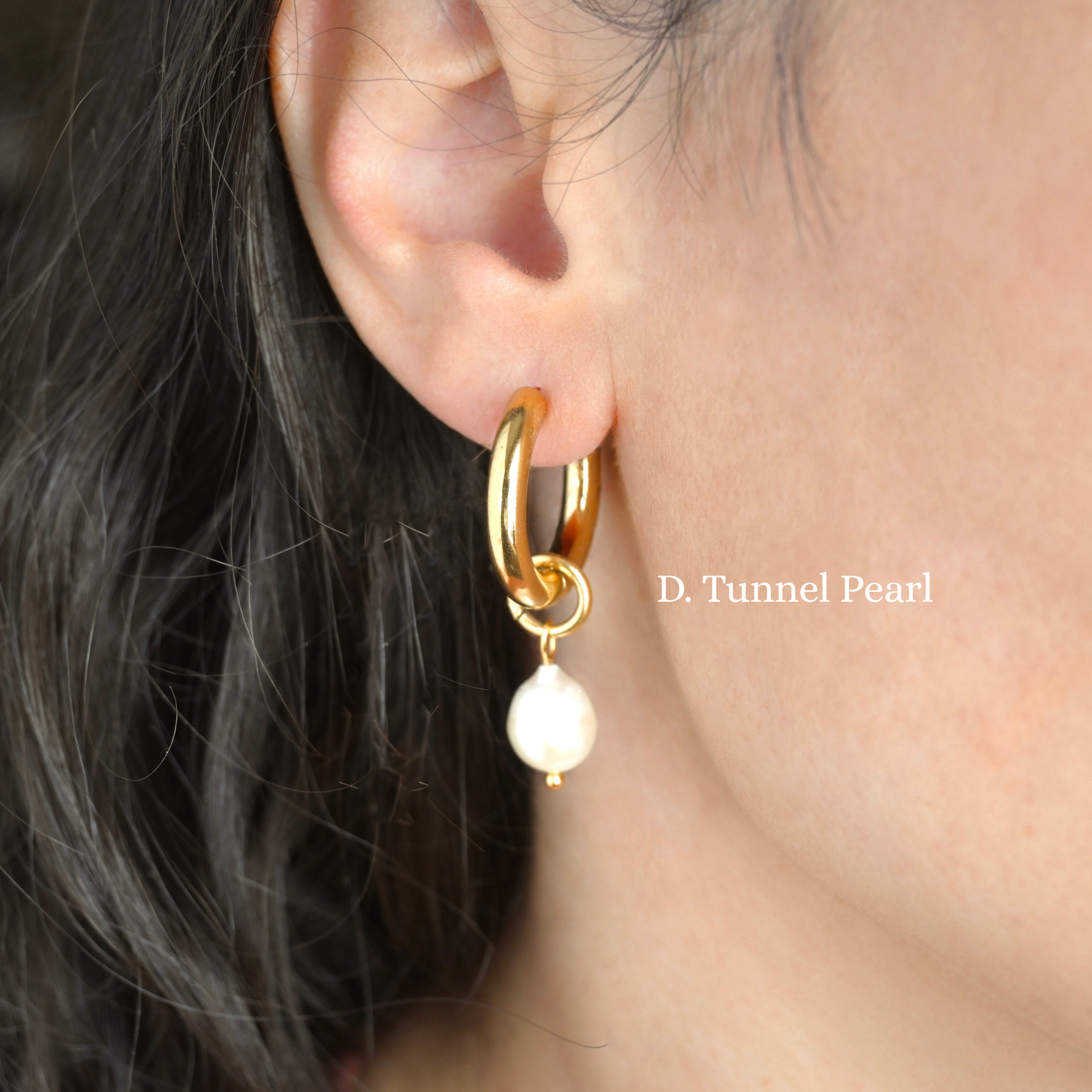 Thick gold hoop earring with a pearl charm worn by a person.