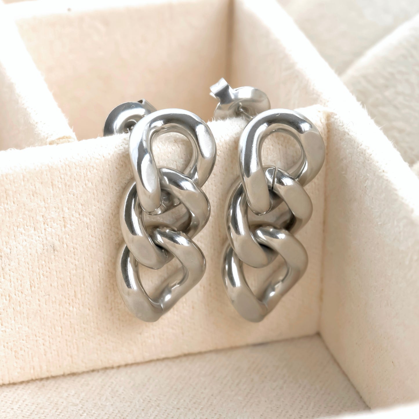 Pair of silver chain-link earrings on a beige quilted surface