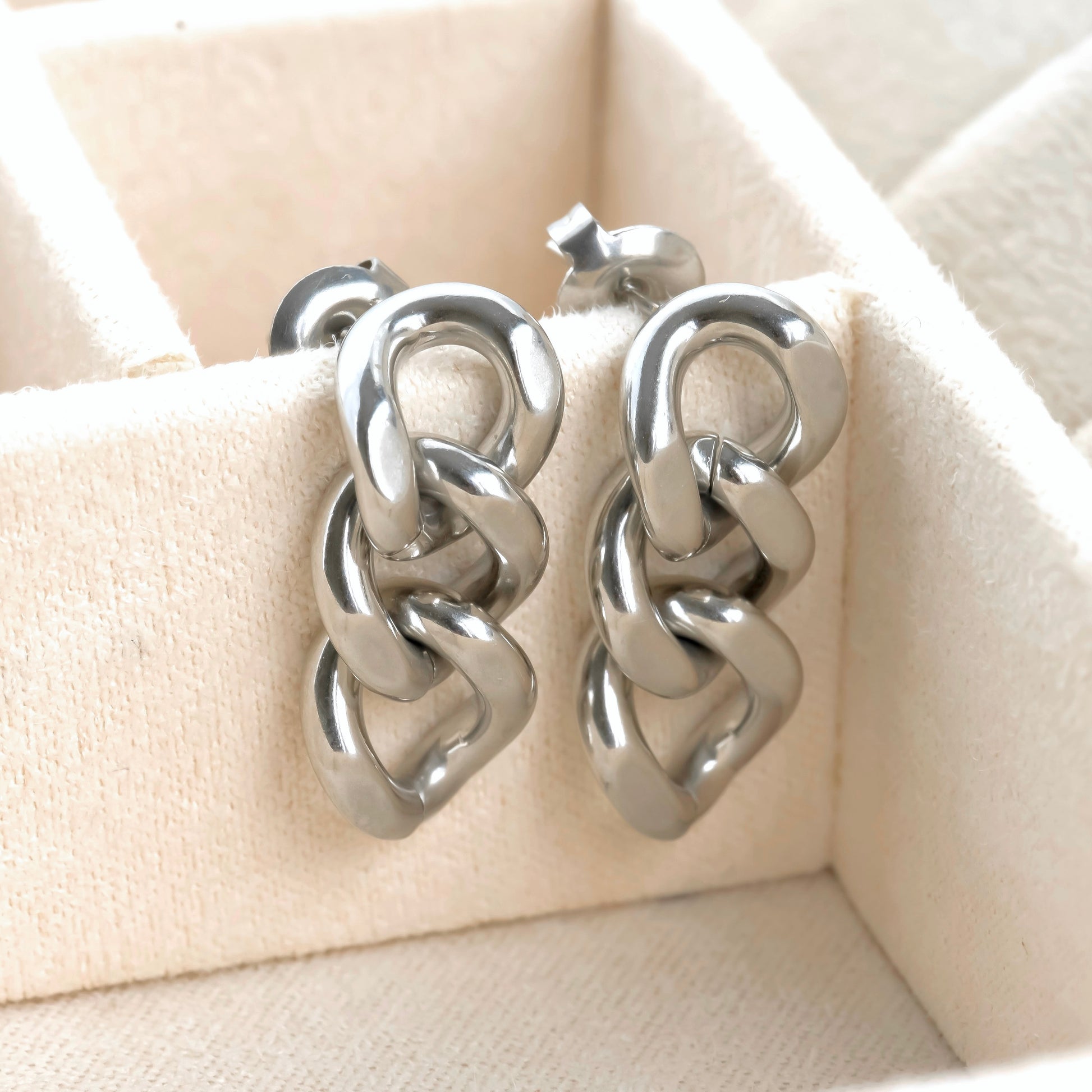 Pair of silver chain-link earrings on a beige quilted surface