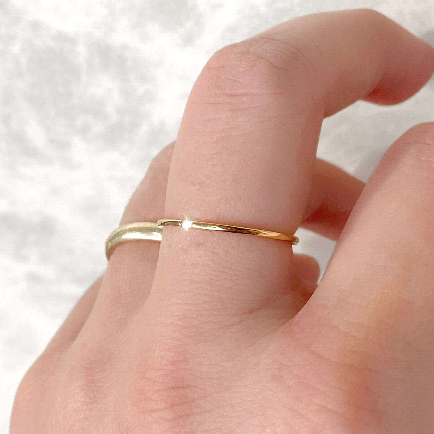 Ultra thin gold ring with a single CZ stone accent in the front on a finger against a neutral background