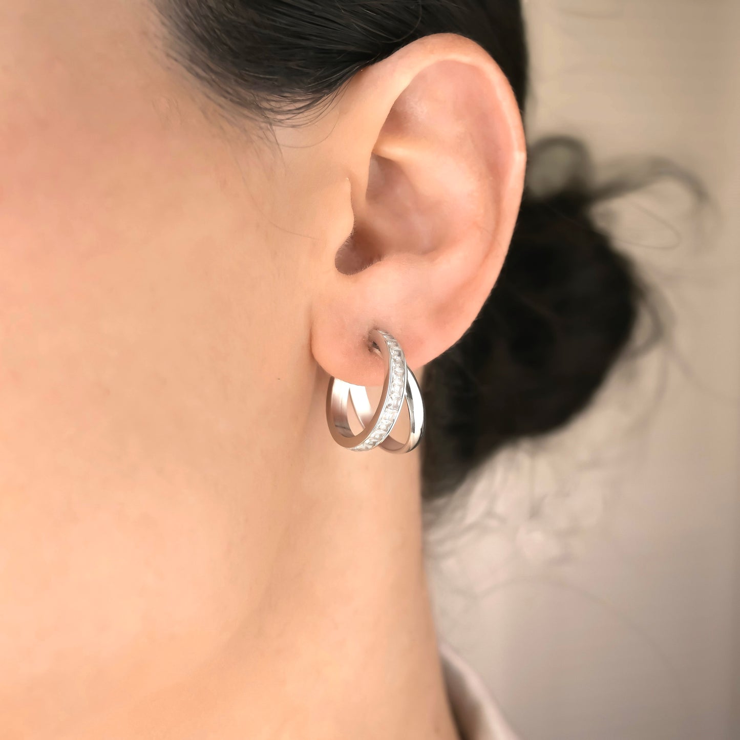 Silver double hoop earrings worn by a person with a neutral background