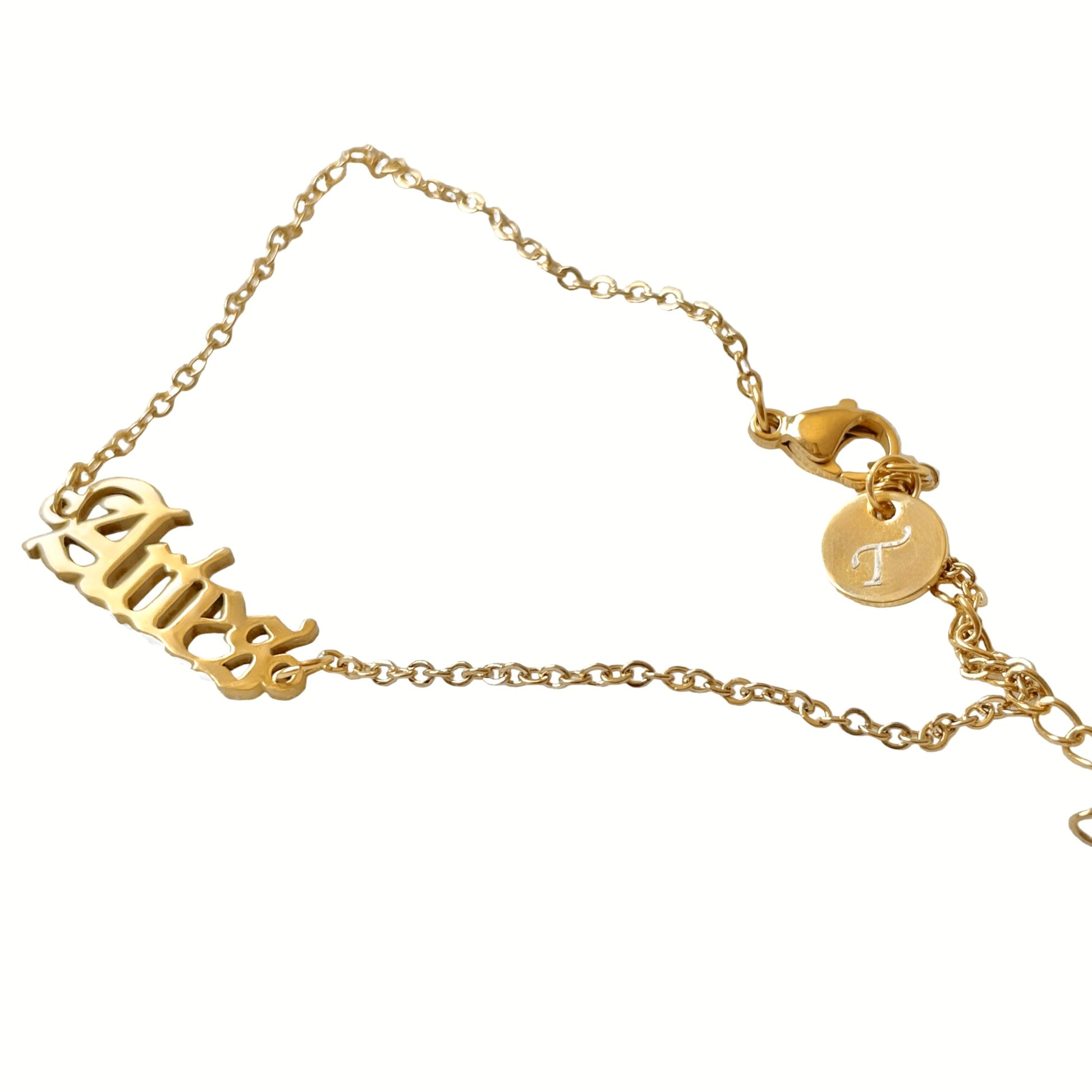 Gold ankle bracelet with 'Aries' and a circular  letter charm at the clasp on a white background
