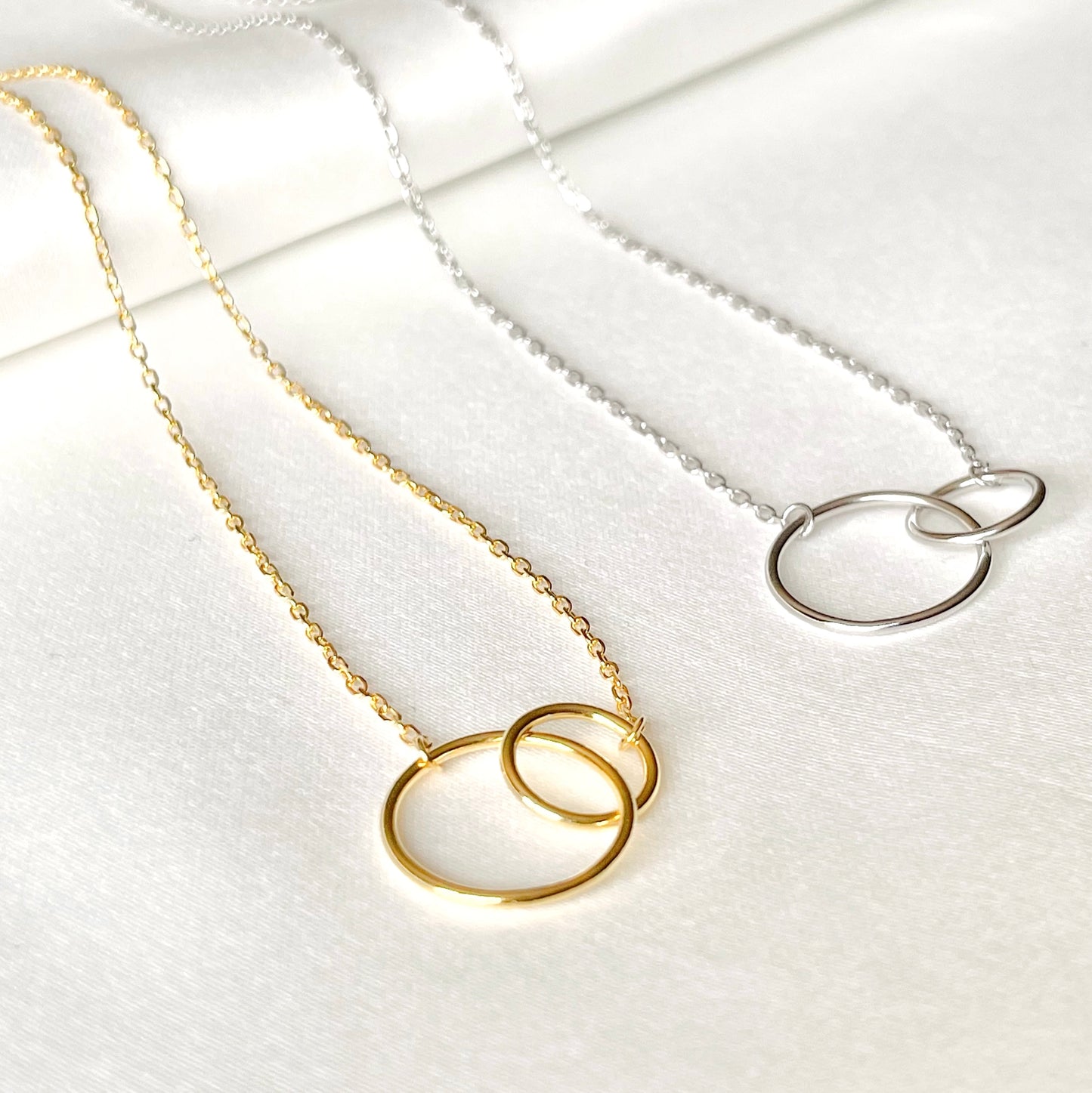 Gold and silver necklaces with  interlocked circular pendants on a white background