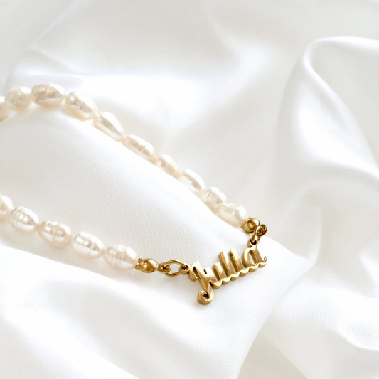 A personalized pearl necklace with a gold nameplate charm spelling 'Julia', displayed on a draped white satin fabric.