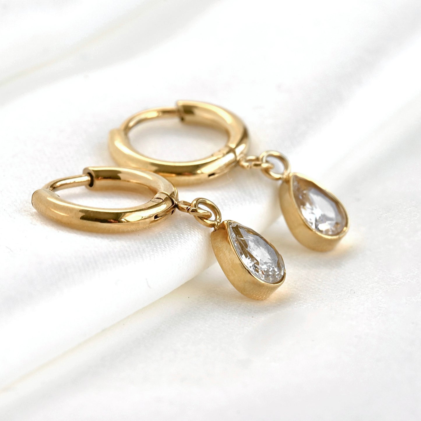 Gold huggie hoop earrings with teardrop-shaped charm on a white background