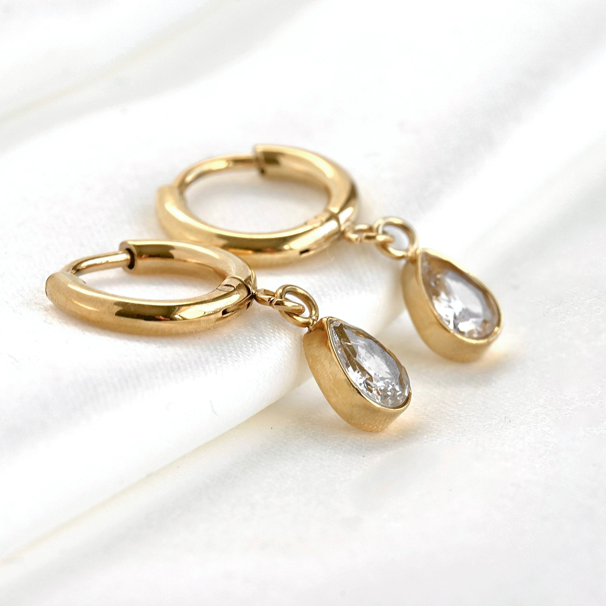 Gold huggie hoop earrings with teardrop-shaped charm on a white background