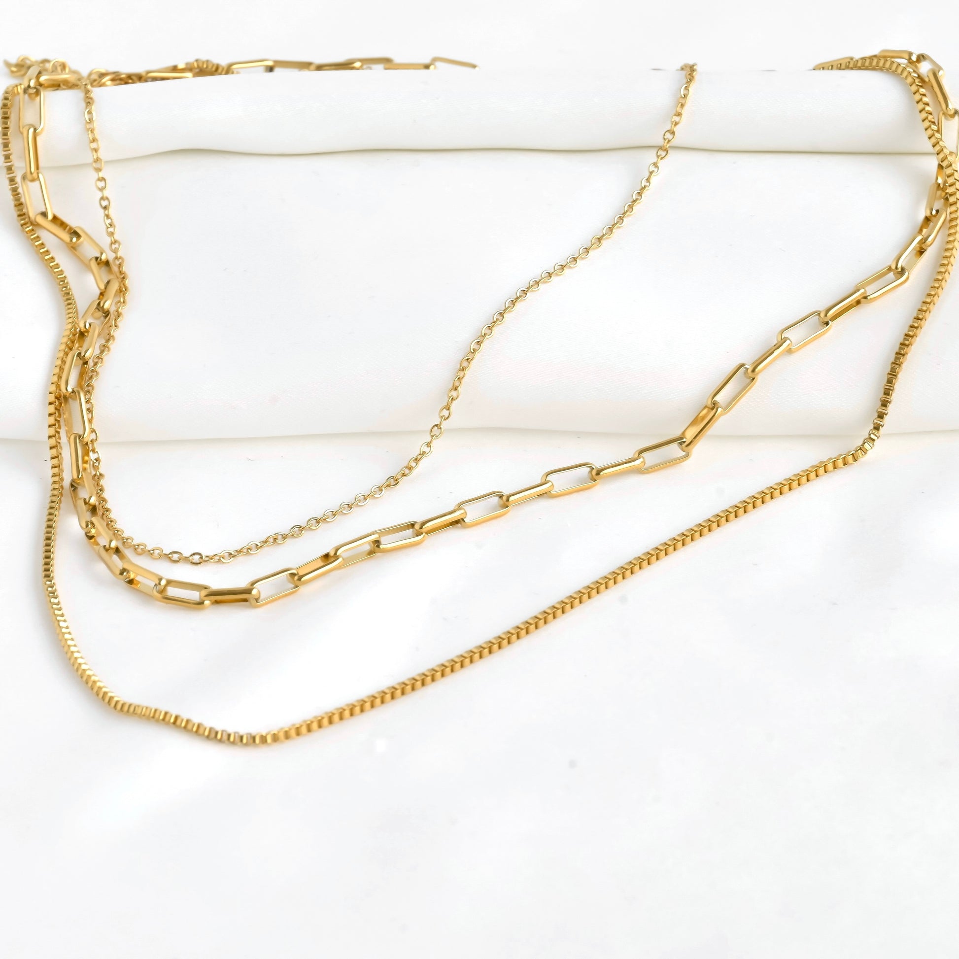 Three gold chains, one box, one small bold paperclip and one fine cable stacked on a white surface